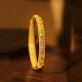 Pulsera tipo brazalete con piedras preciosas verdes doradas y patrón floral de estilo étnico.